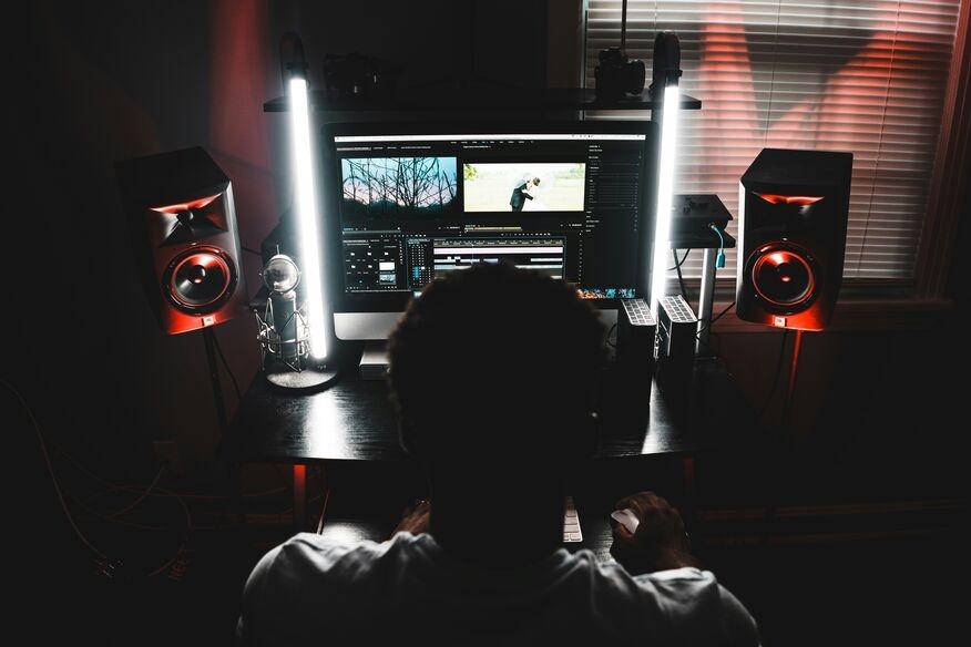 A person editing video on a computer, surrounded by glowing studio lights and speakers, conveying a focused and creative atmosphere.